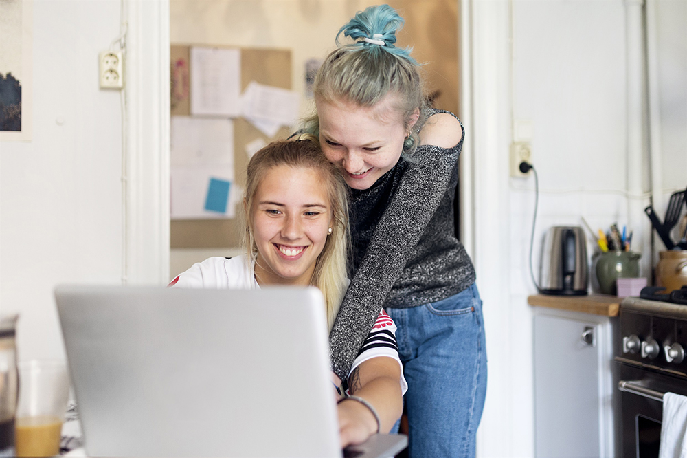 Två tjejer står i köket framför en dator.